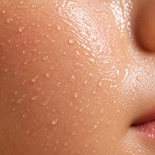 Close-up macro view of healthy, dewy human skin with visible natural texture and pores, covered in many tiny water droplets that create a fresh, hydrated glow.