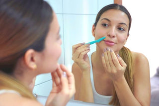 woman looking at herself in the mirror and performing dermaplaning on her face