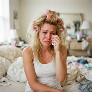 image of a tired and upset woman sitting on a bed surrounded by messy bedroom