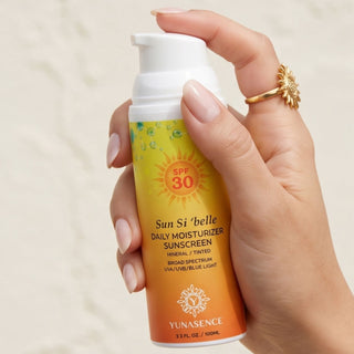 A hand holding a pump bottle of YUNASENCE Sun Si 'belle Daily Moisturizer Sunscreen SPF 30. The bottle has a white pump and a label that transitions from yellow to orange, with a sun graphic and SPF 30 text.