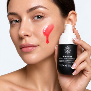 A close-up of a woman holding a black and white pump bottle of YUNASENCE LA NOUVEL Cellular Nutriserum, with a glossy red swipe of the serum on her cheek against a clean white background.