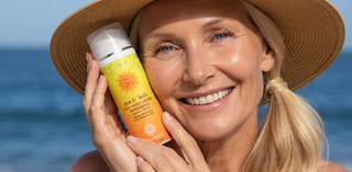 A smiling blonde woman wearing a straw hat holds a bottle of  Sunscreen Lotion against an ocean background.