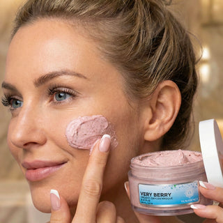 A woman applies a pink berry facial mask from a jar labeled 'VERY BERRY' to her cheek, holding the open jar in her other hand.