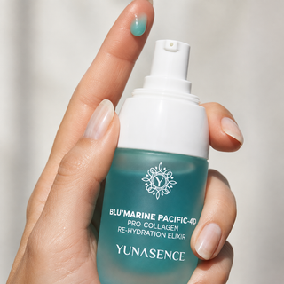 A hand holding a bottle of YUNASENCE Blu'Marine Pacific-40 Re-Hydration Elixir bottle against light background