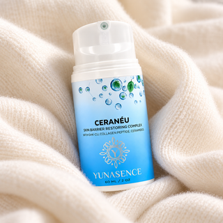 A bottle of YUNASENCE CERANÉU Skin Barrier Restoring Complex cream, featuring a blue and white label resting on a soft, cream-colored knit blanket.