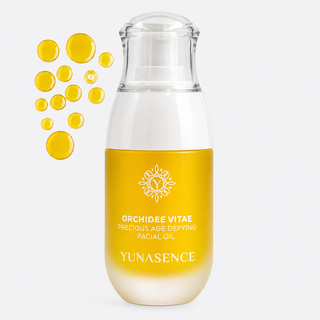 Yunasence Orchidee Vitae Precious Age Defying Facial Oil in a clear bottle  shown on a light gray background with floating golden oil droplets.