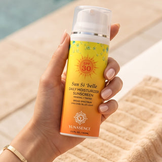 A hand holding a bottle of YUNASENCE Sun Si 'belle Daily Moisturizer Sunscreen SPF 30, set against a blurred background of a pool and a towel.